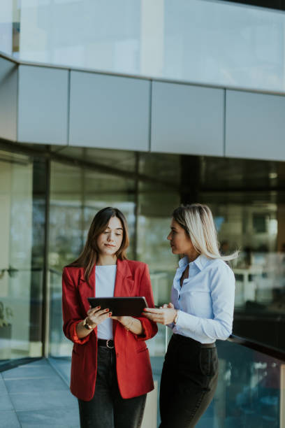istock Two businesswomen discuss strategy outside modern office building in daylight 2155485003
