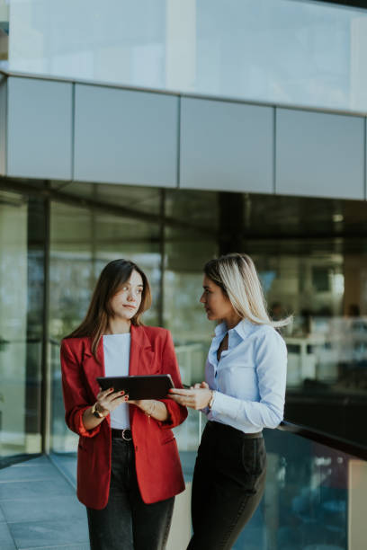 istock Two businesswomen discuss strategy outside modern office building in daylight 2155485009