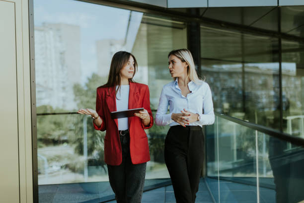istock Two businesswomen discuss strategy outside modern office building in daylight 2155485060