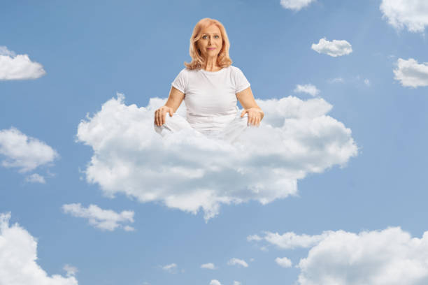 istock Middle aged woman in white clothes practicing yoga on a cloud 2155485404