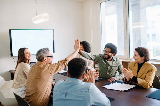istock A spirited office team engages in a high-five, highlighting the successful collaboration and energetic atmosphere in the workplace. The image captures the essence of teamwork and the collective success that comes from a well-coordinated effort. 2155493412