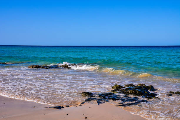 The ocean is calm and the sky is clear. The beach is rocky and the water is a beautiful shade of blue, image