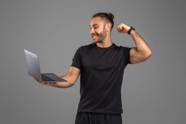 Man Holding Laptop and Flexing Muscles On Grey Background