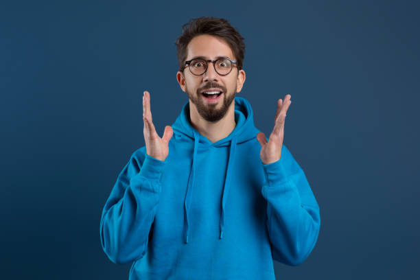 istock Enthusiastic young man with beard and glasses expressing astonishment with raised hands 2155498480