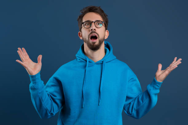 istock Shocked young man with beard and glasses raising hands in amazement 2155498502