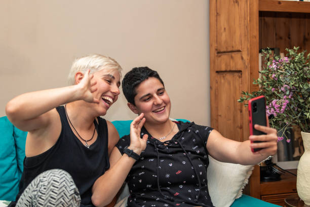 Lesbian couple making smartphone video call with friends from home