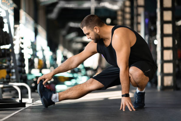 istock Handsome young man performing leg stretch before workout in gym 2155498604