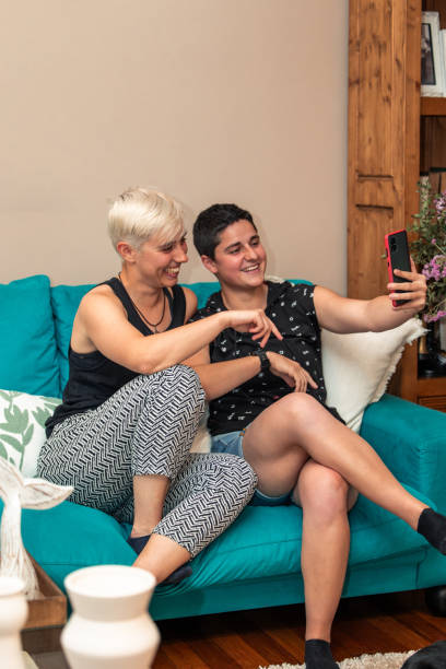 istock Lesbian couple making relaxed video call on cellphone while sitting on home sofa 2155498669