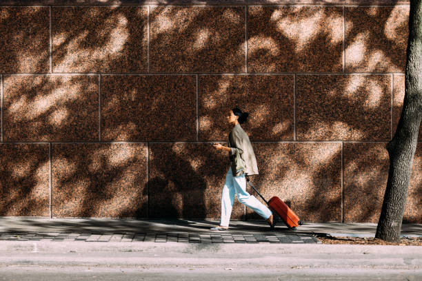 istock Traveler Walking With Suitcase Along A Tree-Lined Sidewalk 2155498715