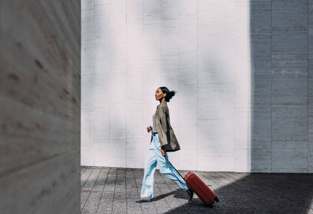 Confident Woman Walking with Red Suitcase in Modern Urban Setting Confident woman walking with red suitcase against a modern urban wall. Ideal for travel, business, and lifestyle concepts. pace yourself photos stock pictures, royalty-free photos & images