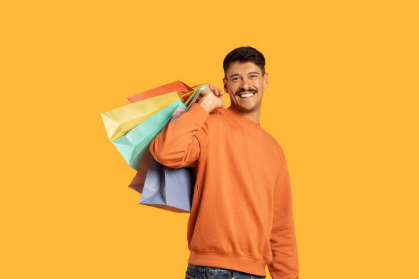 Smiling guy holding various shopping bags on yellow