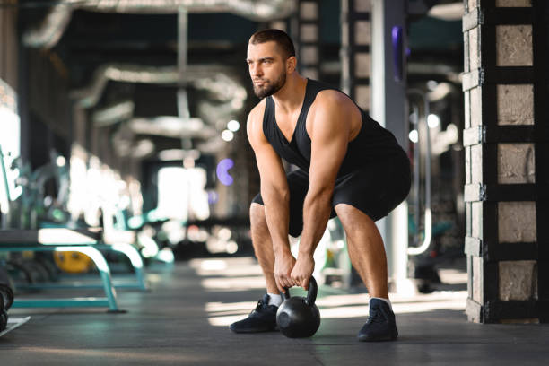istock Motivated Muscular Man Training With Kettlebell At Modern Gym Interior, 2155499053