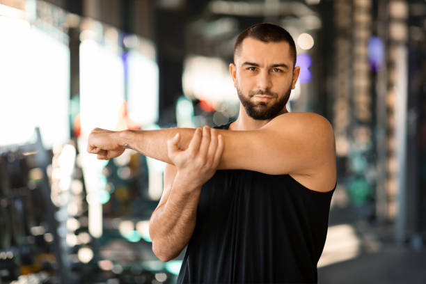 istock Man Stretching Arms Before Workout at a Sunny Gym 2155499084