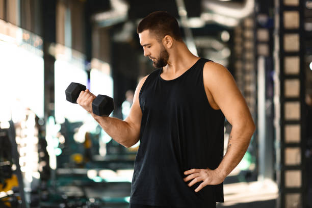 Muscular Man Performing Dumbbell Curls at Gym During the Day