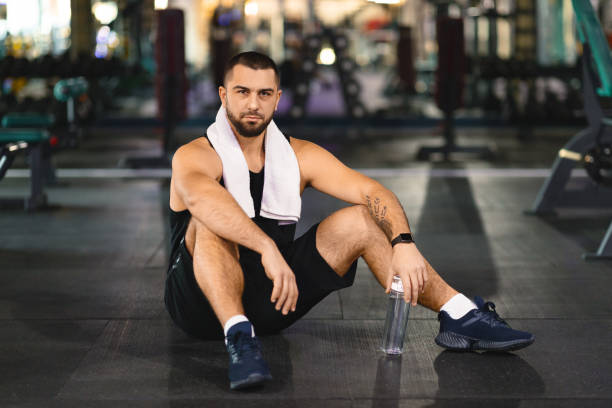 istock Man Sitting on the Ground in a Gym 2155499148