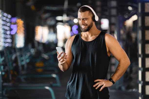 istock Smiling Man Choosing Music on Smartphone at a Modern Gym 2155499166