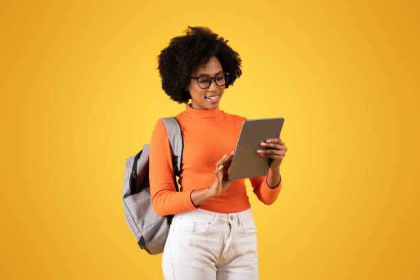 istock A young woman with glasses and curly hair, smiling while using a tablet, wearing an orange turtleneck and backpack 2155499466