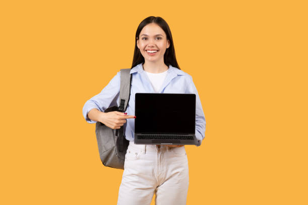 istock Smiling female student with laptop pointing at blank screen 2155499800