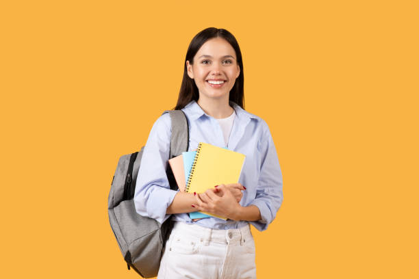 istock Smiling female student with notebooks and backpack on yellow background 2155499804
