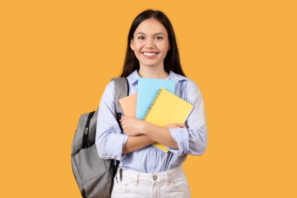 istock Young Woman Embracing Notebooks with Joy, yellow background 2155499909