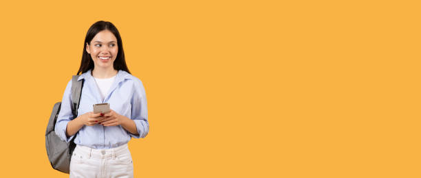 istock Smiling female student with phone and backpack looking at free space 2155499942