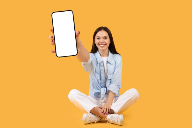 istock Smiling woman showing smartphone screen, sitting crossed-legged 2155500007