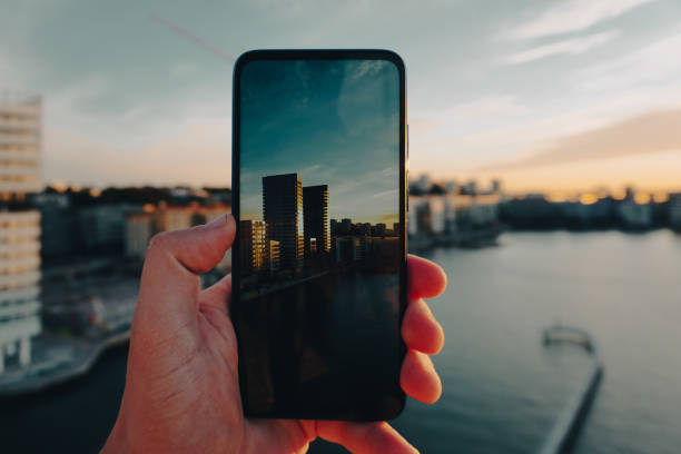 Cropped hand holding a mobile phone while photographing cityscape