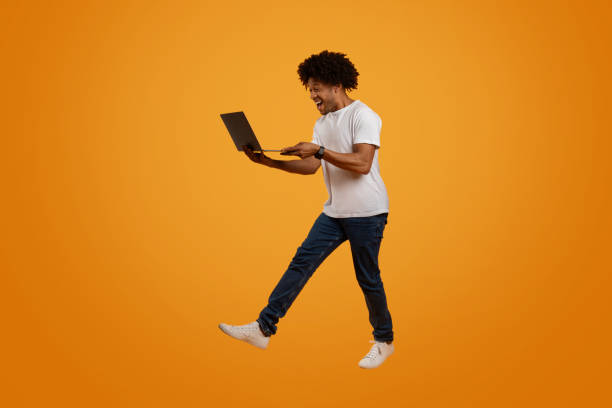 istock Excited millennial african american guy jumping with laptop 2155500354