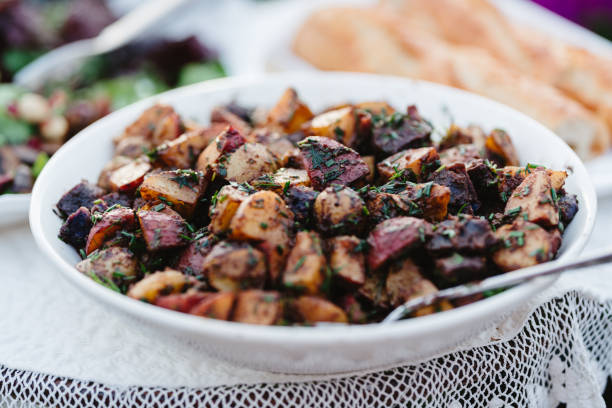 An appetizing plate of cooked potatoes sit on an outdoor table ready to be eaten during a friendly potluck.