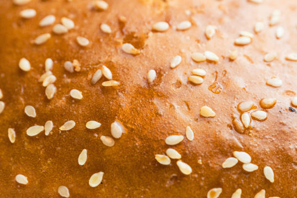 Sesame seed bun, showcasing the scattered seeds on the golden brown surface. The seeds are scattered across the surface of the bun, creating a pleasing texture, an extreme close-up macro shot.