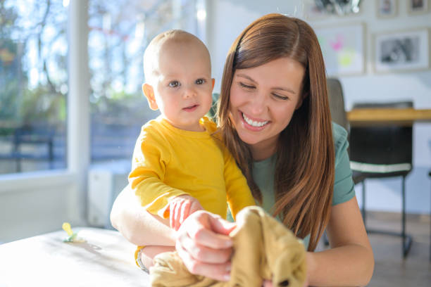 A cheerful woman enjoys quality time with her baby at home, both dressed casually, with natural light enhancing the serene setting.