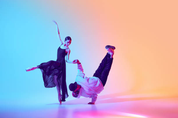 istock Classical ballerina and a contemporary street dancer making breathtaking creative performance, dancing against gradient background in neon light 2155514566