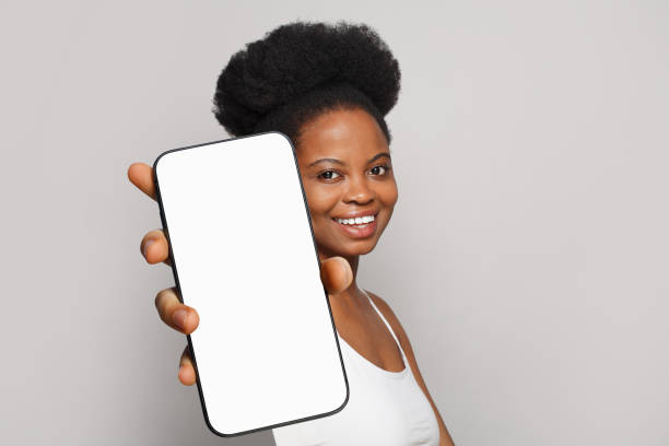 istock Good-looking healthy woman holding smartphone with white empty blank screen display on gray studio wall background. Happy model with phone 2155517990