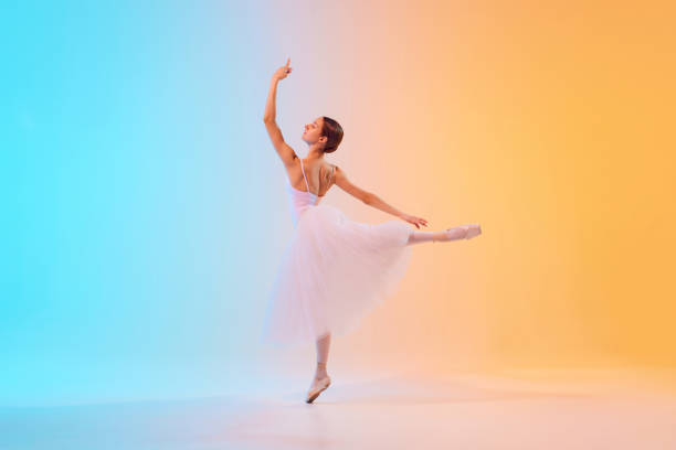 istock Dynamic photo of ballet dancer extends her arm elegantly dressed in pale tutu in neon light against blue-orange gradient background. 2155519716