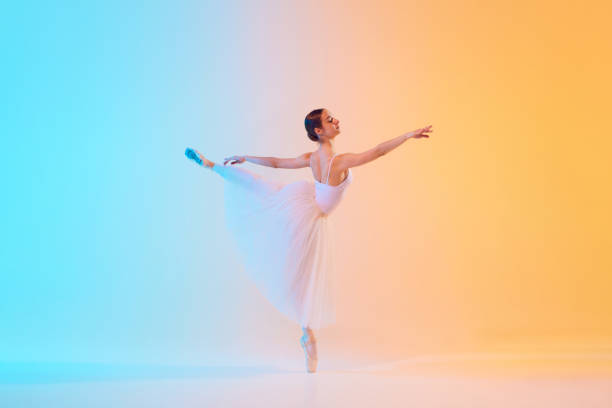 istock Elegant ballet dancer in white ensemble gracefully extends in neon light against blue-orange gradient background. 2155519720