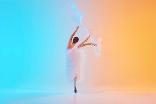 Elegant ballet dancer in white ensemble gracefully move with fabric in neon light against blue-orange gradient background. Concept of art, movement, classical and modern fusion, beauty and fashion. Ad