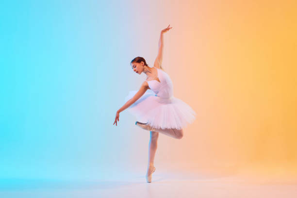 istock Graceful and poised young ballet dancer performs dance moves in action in neon light against blue-orange gradient background. 2155519734