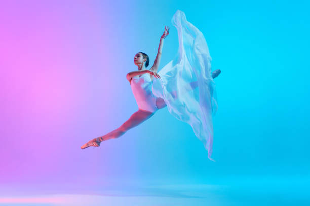 istock Ballet dancer performs jumping split in motion with flowing white cloth in neon light against vivid gradient background. 2155519747