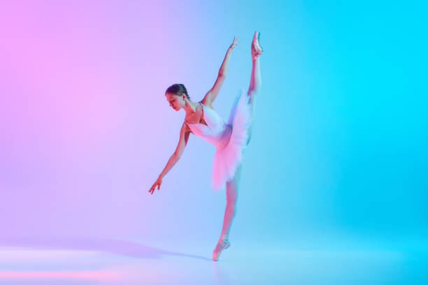 istock Art through motion. Young ballerina in white tutu doing arabesque in motion in neon light against vivid gradient background. 2155519774