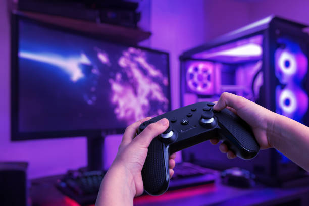 istock Immersive gaming setup featuring a gamer playing on a gaming PC with a gamepad, set in a gamer room with a gaming desk and LED lights 2155520108