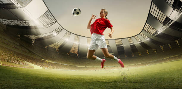 istock Dynamic image of competitive young woman, soccer player on field during game, hitting ball with chest. Open air 3D stadium. 2155520745