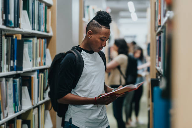 istock Young black man reads a book in the library 2155522580