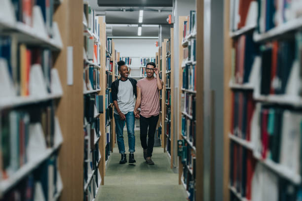 istock Gay couple holding hands and walking through library 2155522590