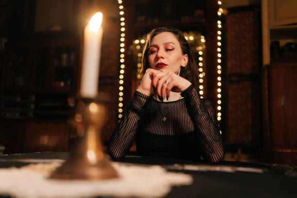 istock Low-angle portrait of female soothsayer dealing Tarot cards forecasting future for client by light of burning candles. Fortune-telling having divination session with tarot cards 2155522867