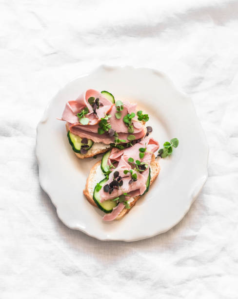 istock Delicious breakfast, snack, tapas - sandwiches with ham, cucumber and microgreens on a light background, top view 2155525111