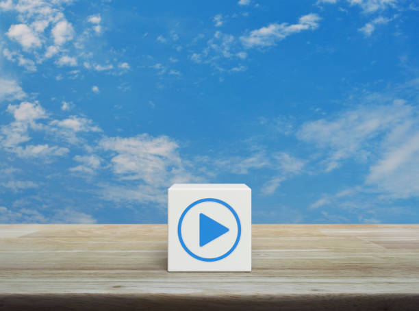 Play button icon on white block cube on wooden table over blue sky with white clouds, Business music online concept
