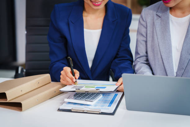 two asian businesswomen collaborate on stock market strategies and financial services, exchanging comments and suggestions on loan applications and investment opportunities. - underwriting fotografías e imágenes de stock