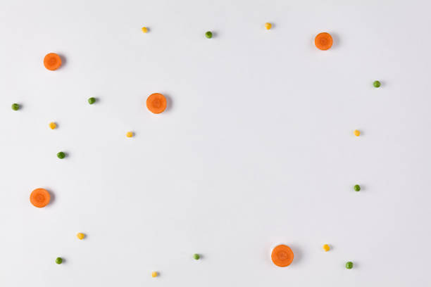 Minimalist Food Ingredient Flat Lay: Fresh Carrot Slices, Green Peas, and Corn Kernels on White Background.