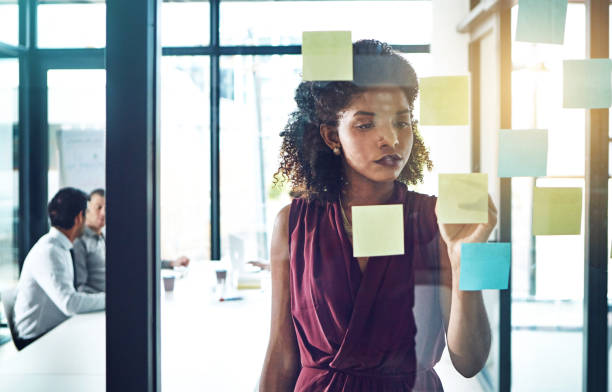 istock Business, woman and writing on sticky notes in office for brainstorming, work schedule and meeting reminder. Professional, employee and ideas on glass in conference room with presentation information 2155530121