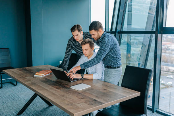 istock A team of three young men hard at work on their laptops in a bustling office. 2155530565